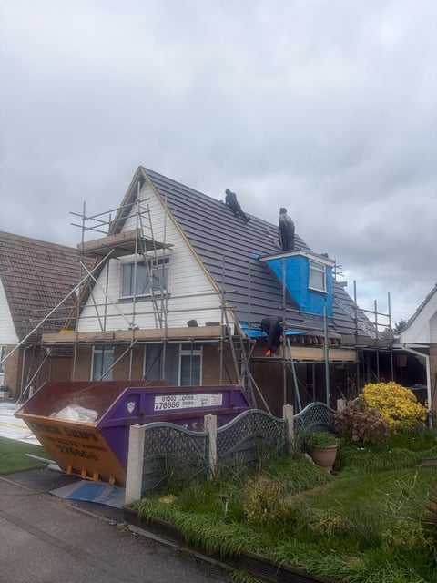 House under renovation with scaffolding, new metal roof, and construction dumpster in front yard