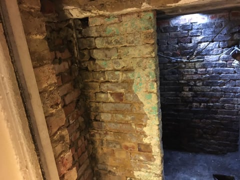 Underground brick corridor with aged walls painted yellow-green on left and dark blue-black on right side