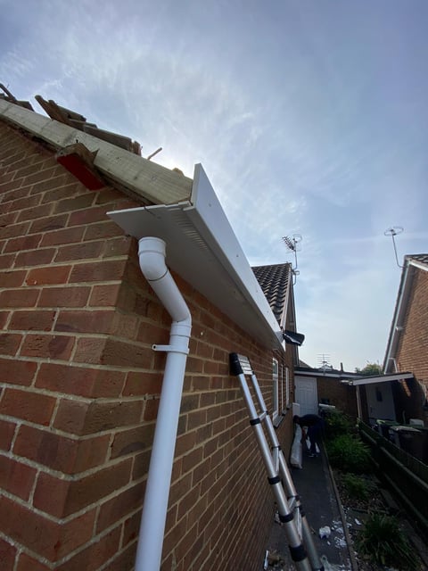 White gutter downspout and fascia board on brick house exterior with blue sky