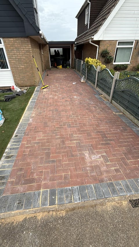Red brick herringbone driveway leading to houses with green gates and lawn on sides