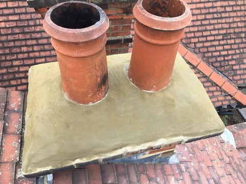 Two terracotta chimney pots mounted on a concrete base on a brick roof