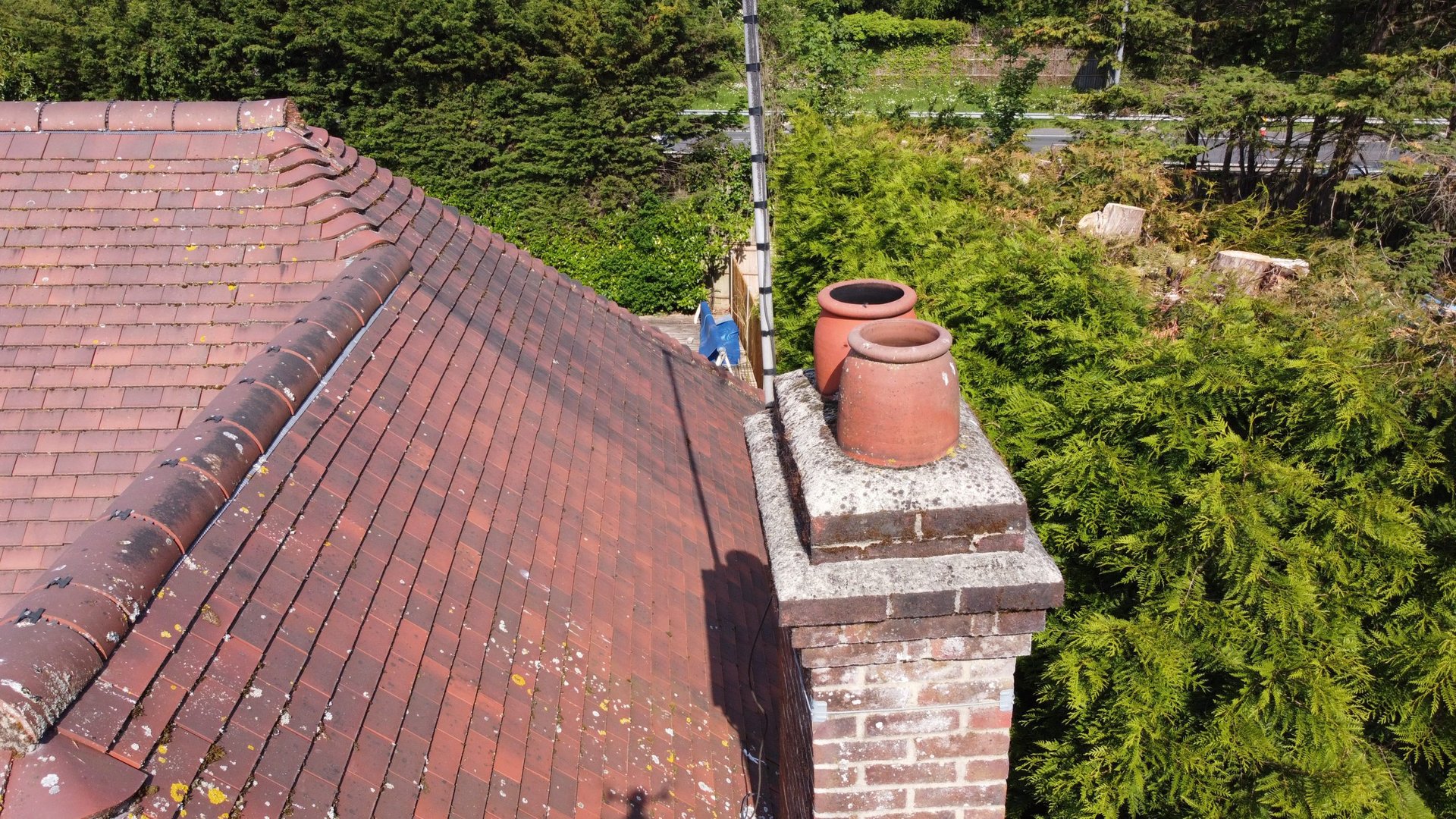 Red tile roof with brick chimney and terracotta pots, aerial view overlooking green vegetation