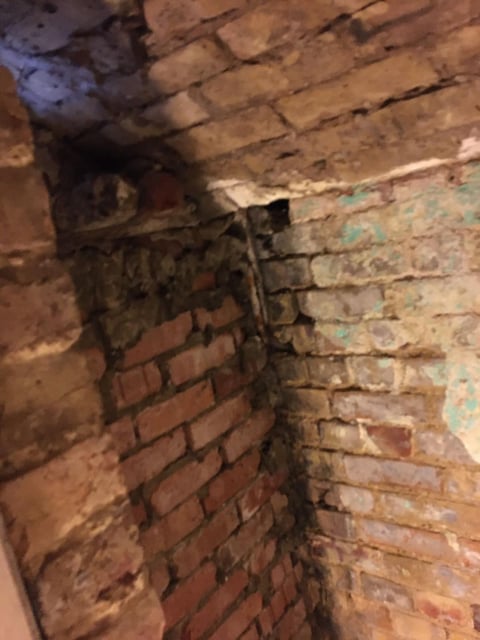 Old metal pipe fixture mounted on a weathered brick wall with peeling paint and mortar decay
