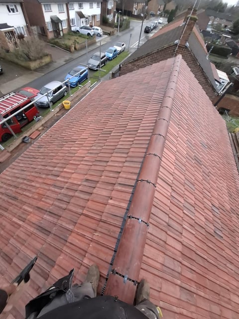 Aerial view of a red tile roof with a metal chimney running diagonally across it, overlooking a residential street with parked cars