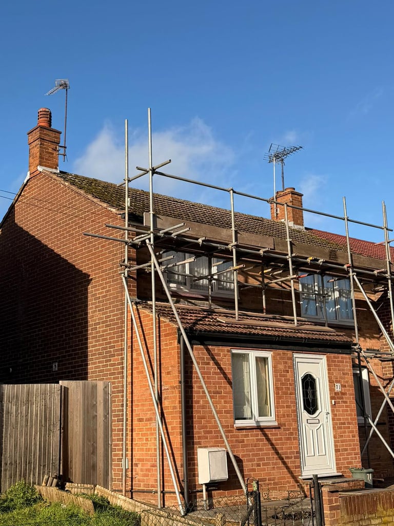 Brick house undergoing renovation with metal scaffolding covering the roof and upper structure against a clear blue sky