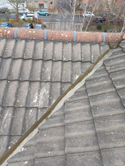 Close-up of roof with gray tiles, metal gutter straps, and residential area with parked cars visible in background