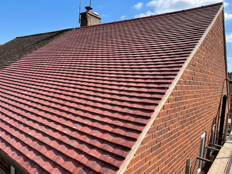 Red tiled roof on brick building with clear blue sky and chimney visible