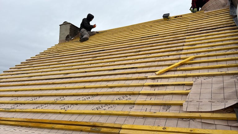 Worker installing yellow insulation and roofing materials on a residential roof under construction