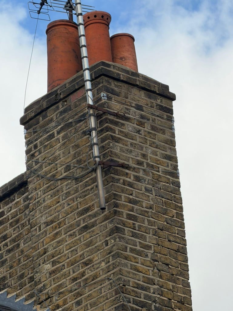Brick chimney with three red clay pots on top and metal straps against a light cloudy sky