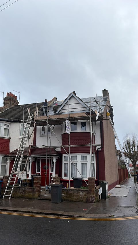 Red and white terraced house undergoing roof repair with scaffolding and ladders on overcast day
