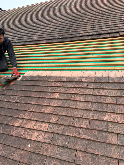 Worker installing colorful roof underlayment on a residential roof with existing dark asphalt shingles