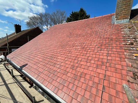 Newly installed red clay tile roof on residential house with clear blue sky and surrounding trees visible