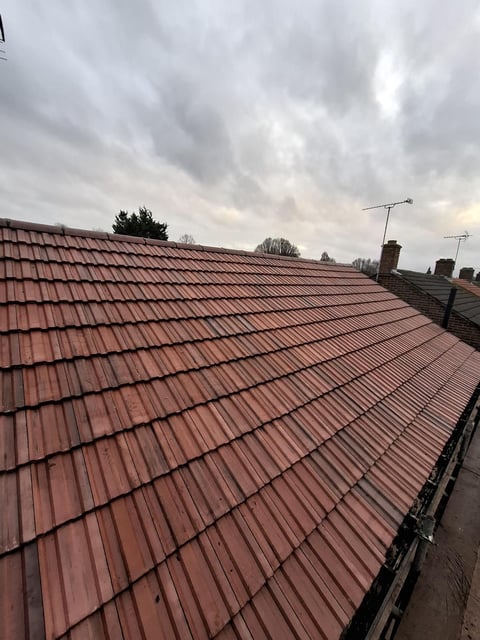 Red tiled roof of a house with chimneys and TV antennas under a cloudy sky