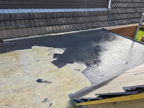 Flat roof being waterproofed with dark membrane coating during construction, partially complete with tan insulation visible